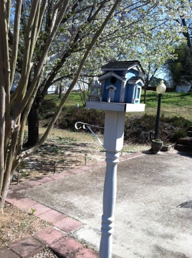 A charming blue birdhouse set on a white post in a serene garden.