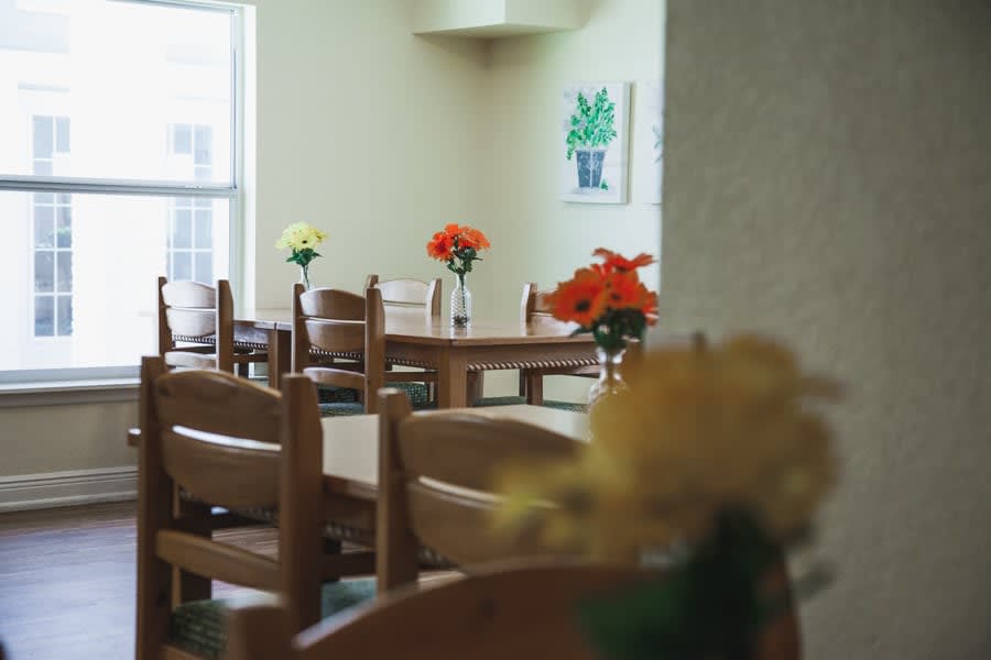 A cozy dining area with wooden tables and chairs, adorned with colorful flowers.