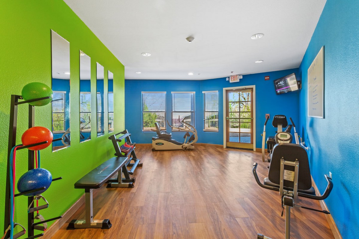 A brightly colored gym with various exercise equipment and wooden flooring.