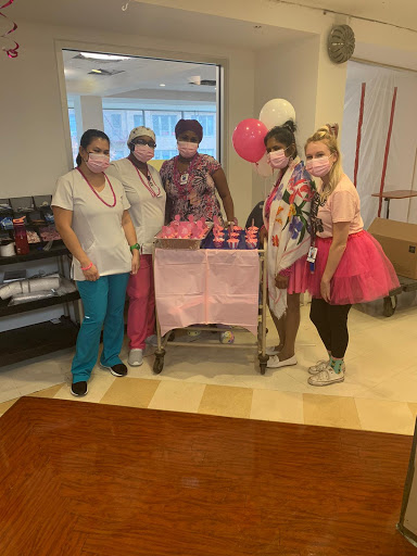 A cheerful gathering of healthcare workers celebrating with pink-themed treats and decorations.