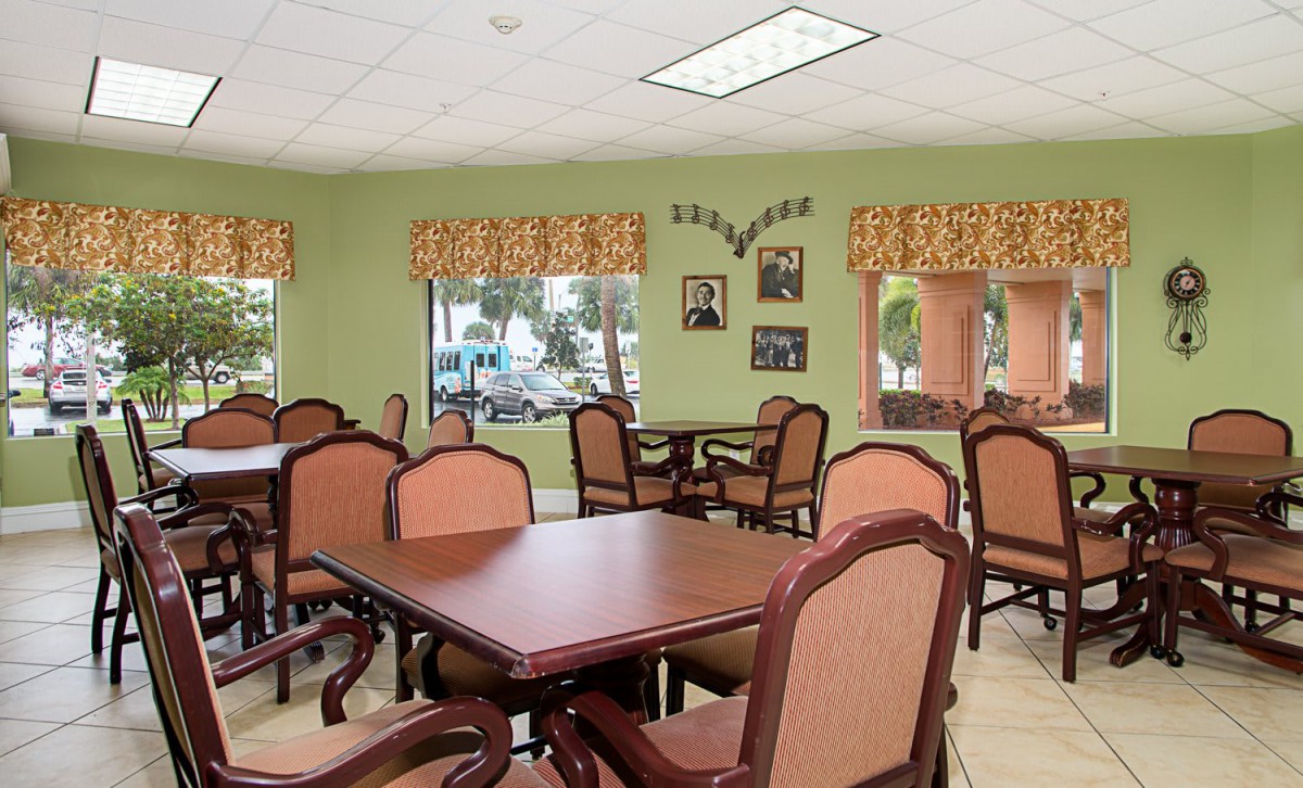 A cozy dining room with multiple tables and chairs, decorated with green walls and patterned curtains.