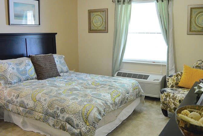 A cozy bedroom interior with a neatly made bed and natural light filtering through the window.