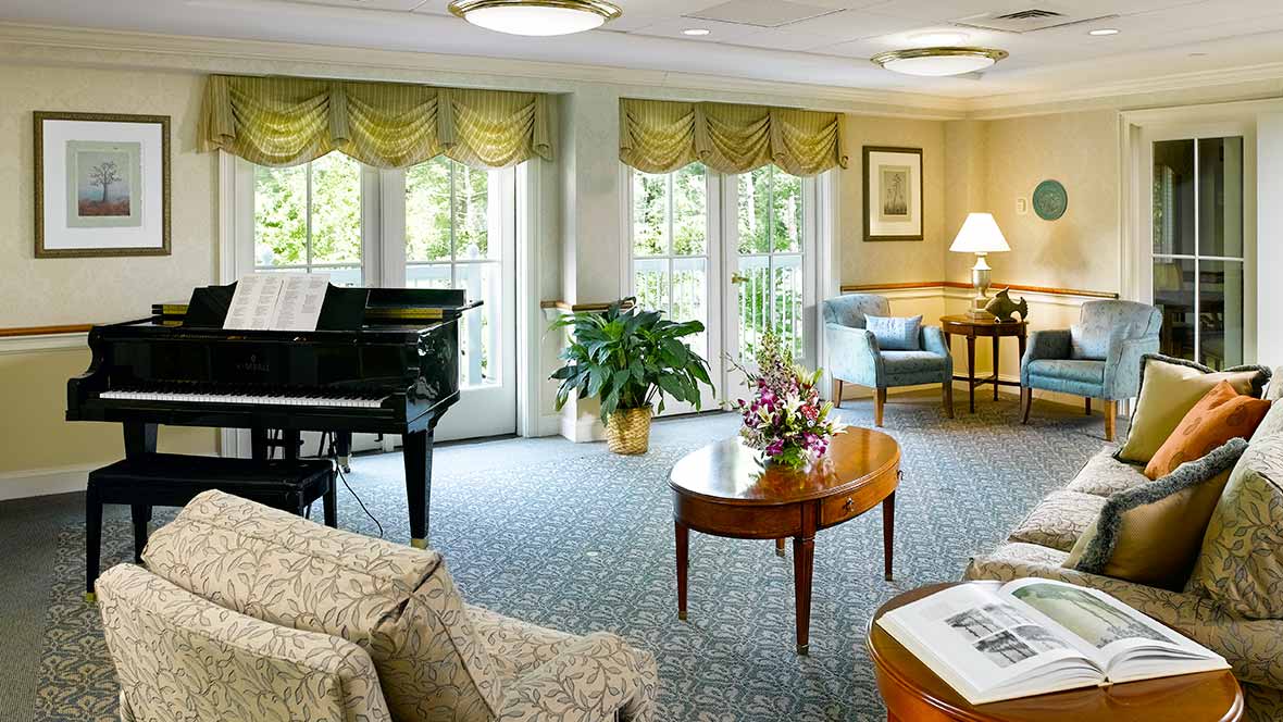 A beautifully decorated living room featuring a grand piano, elegant furnishings, and large windows with curtains.