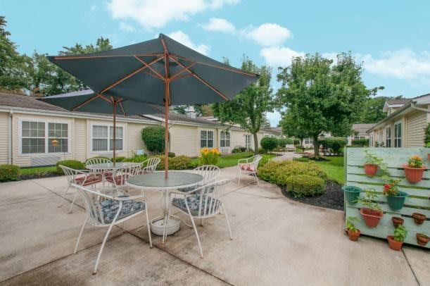 A serene outdoor patio area with a table, chairs, and umbrella surrounded by lush greenery.