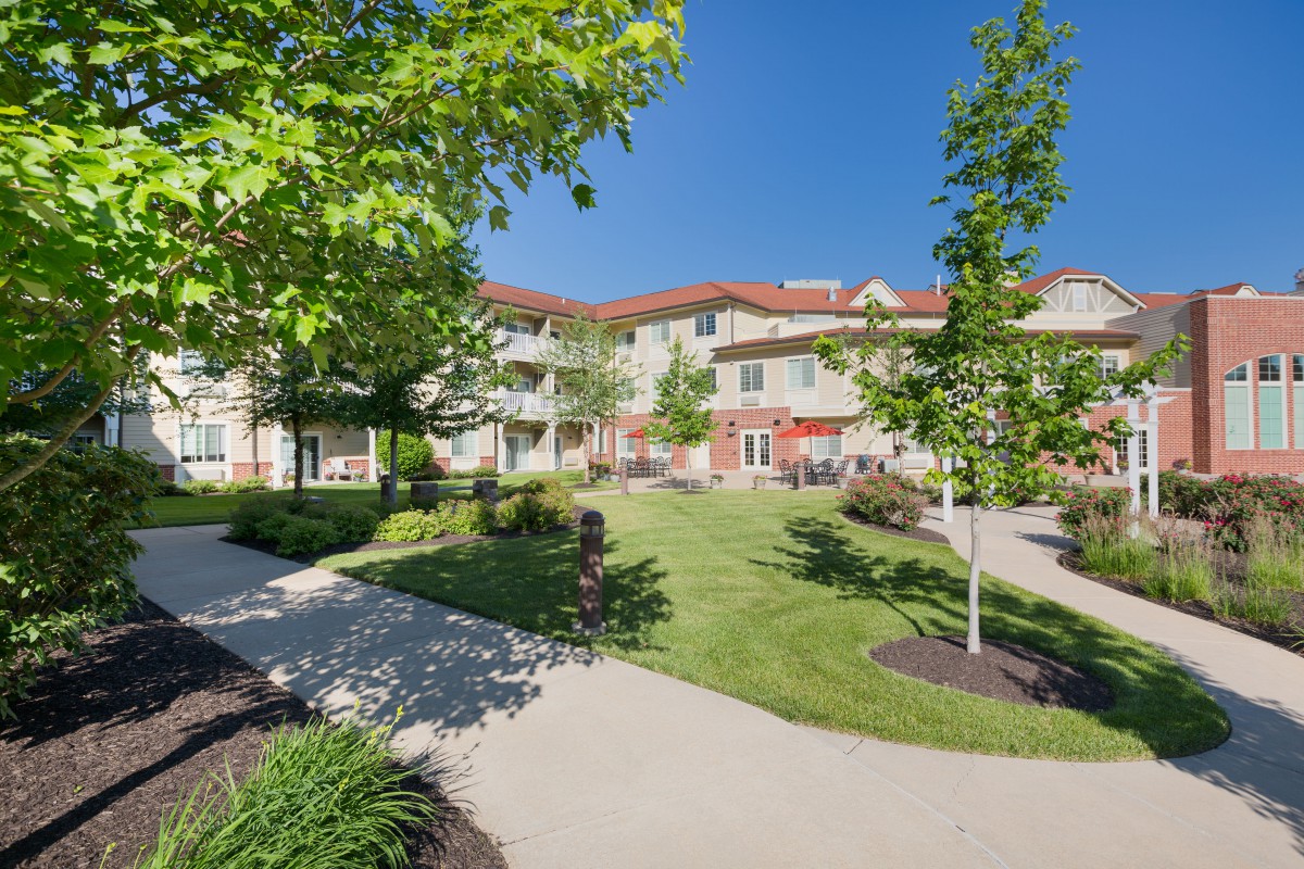 A scenic view of a residential building surrounded by a well-maintained garden with pathways and trees.