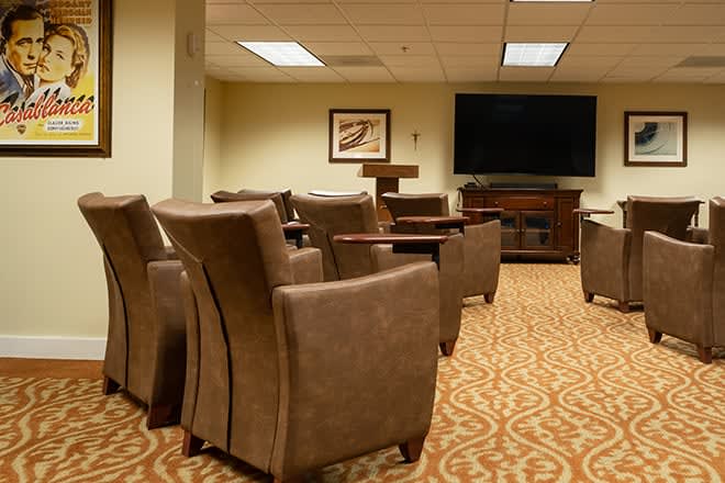 A well-furnished conference room with comfortable armchairs, a large television, and a carpeted floor setup for presentations.