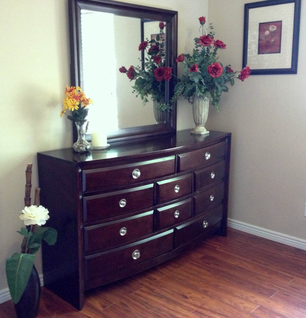 A wooden dresser with a mirror above, adorned with vases of colorful flowers in a neatly arranged room.