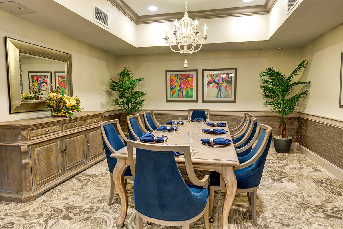 Elegant dining room with a chandelier and blue chairs around a large table.