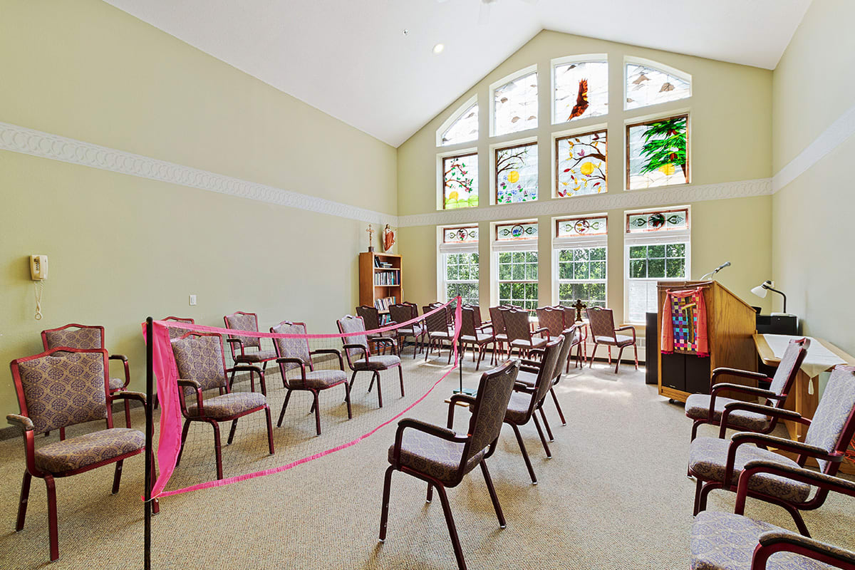 An empty meeting room with chairs arranged in a semi-circle facing large stained glass windows.