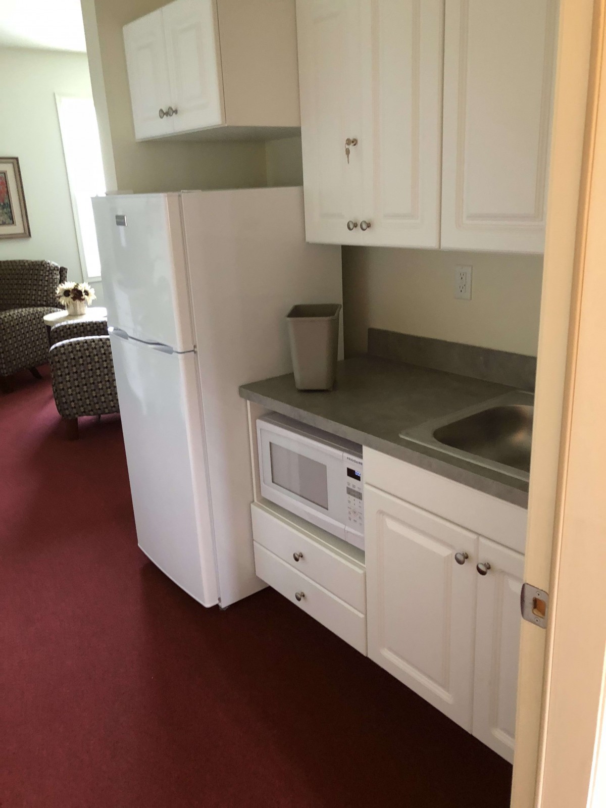 Compact kitchen area with white cabinets, a refrigerator, microwave, and sink.
