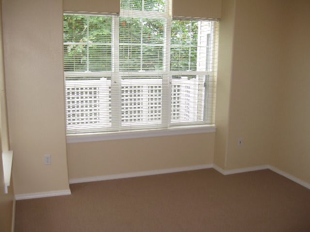 A small, carpeted room with a large window allowing natural light to enter.
