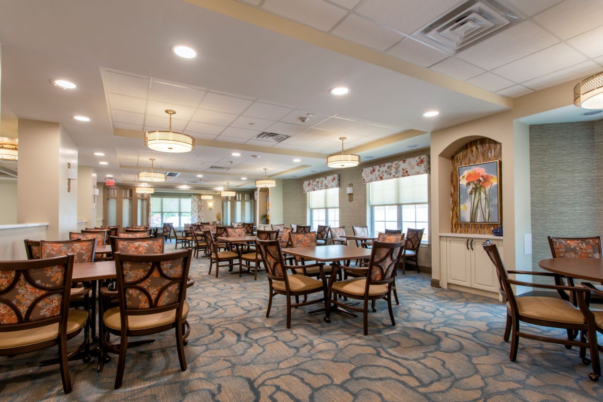 A spacious and elegantly decorated dining room with multiple tables and chairs arranged neatly, featuring large windows that allow natural light to fill the room.