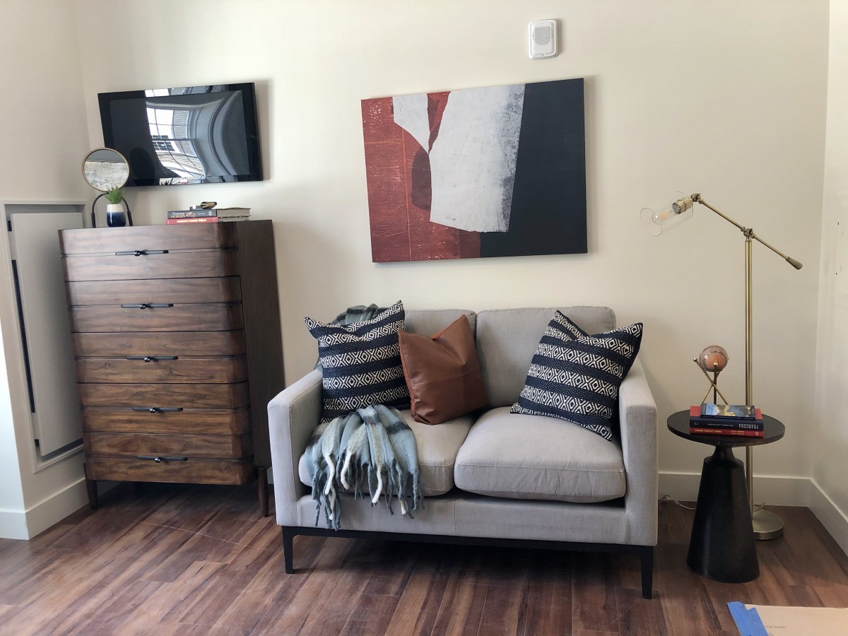 A cozy living room corner featuring a small sofa with patterned pillows, a blanket, and modern artwork on the wall.