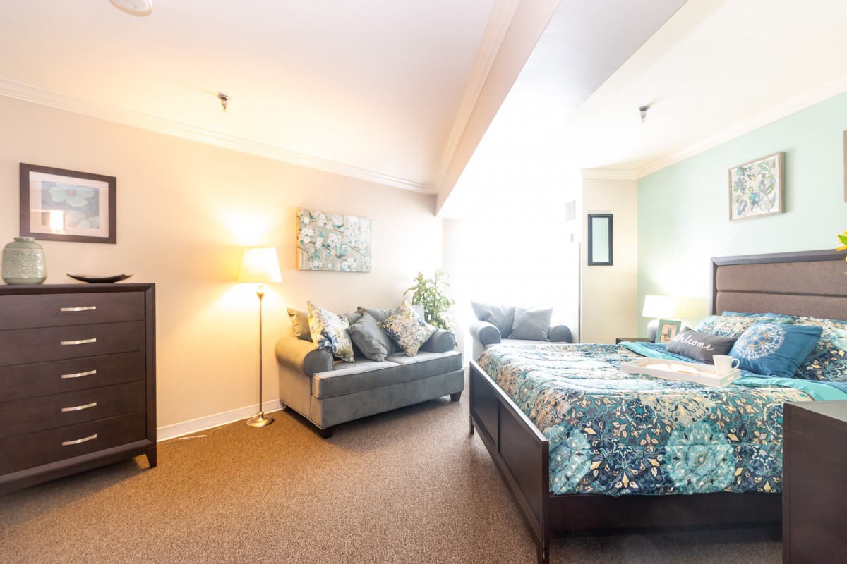 A cozy bedroom with a bed, sofa, and decor in soft lighting.