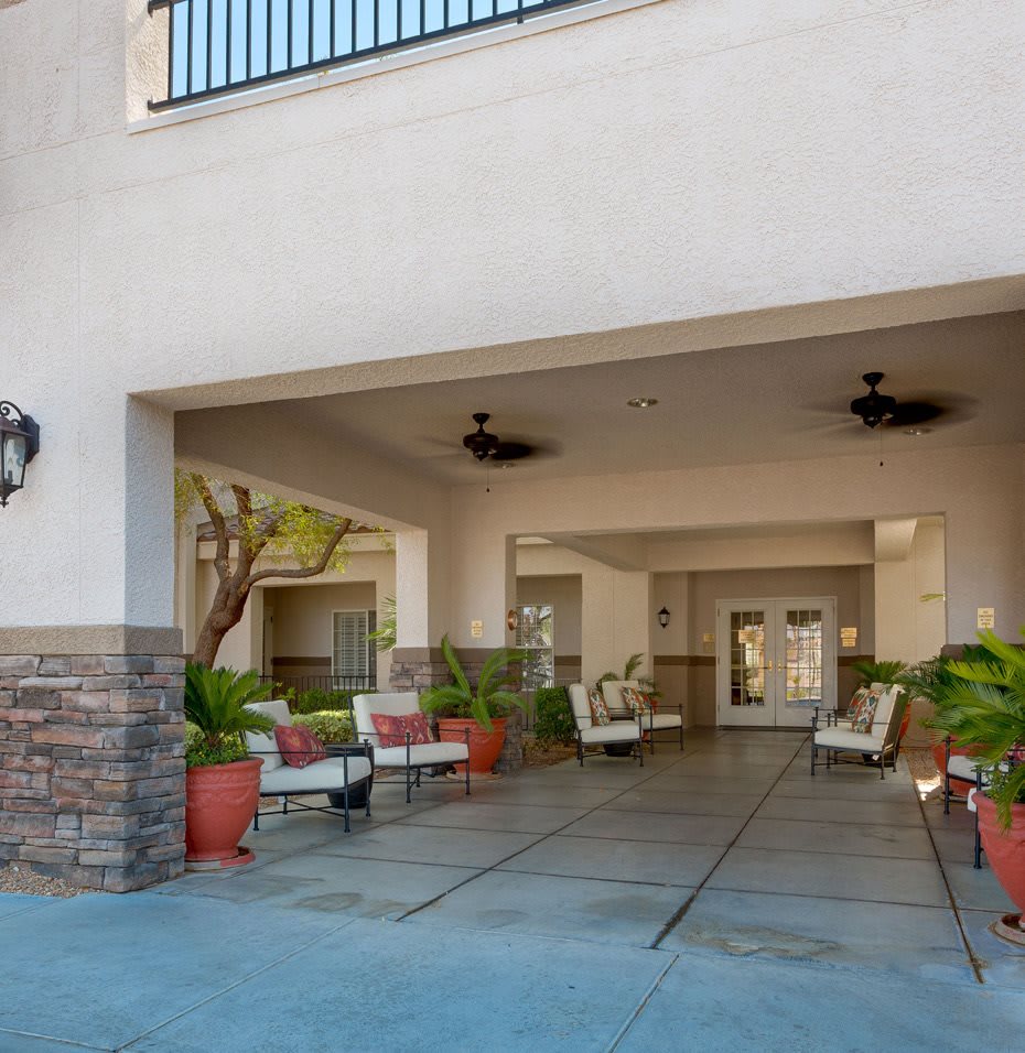 Covered entrance with outdoor seating and plants at a building.
