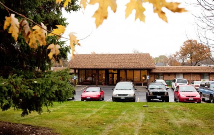A quaint building with a parking lot in front, surrounded by autumn foliage.