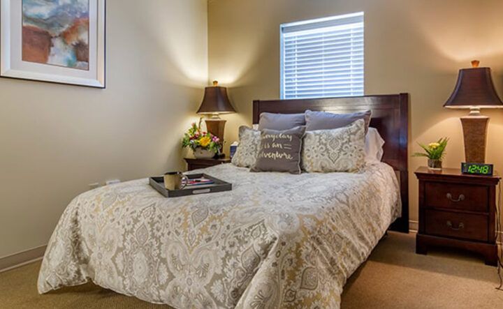 A cozy bedroom with a neatly made bed featuring decorative pillows and a bedside lamp.