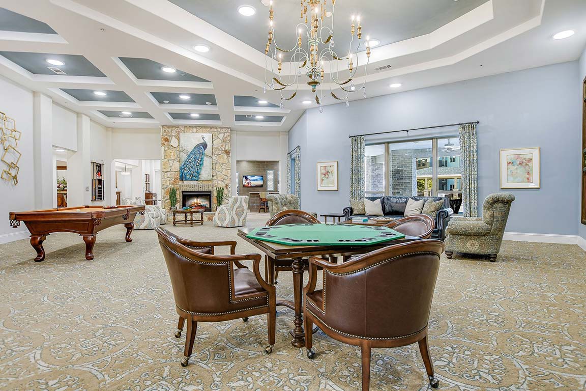 A luxurious recreation room with a card table, plush chairs, a pool table, and a chandelier.