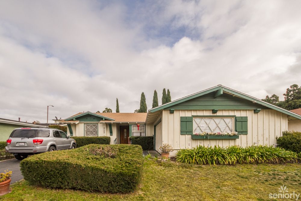 A suburban house with a well-maintained lawn and shrubs under a cloudy sky.