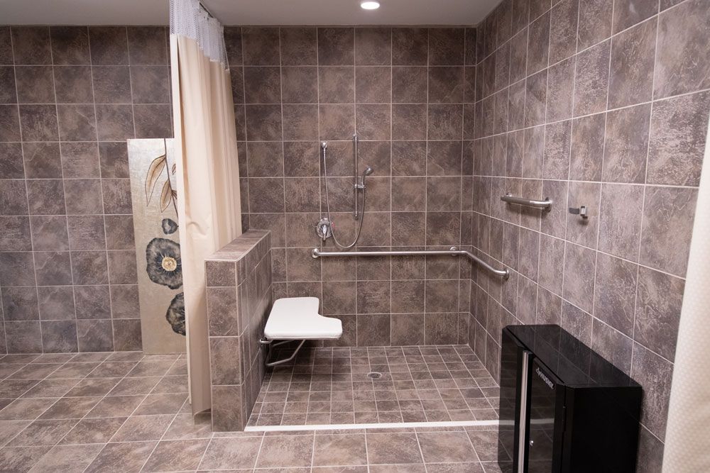 An accessible bathroom with a tiled shower area, equipped with grab bars and a folding shower seat.