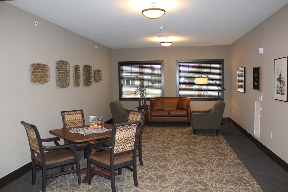 A cozy living room with a seating area, including a sofa, chairs, and a table. The space is well-lit with natural light coming through the windows.