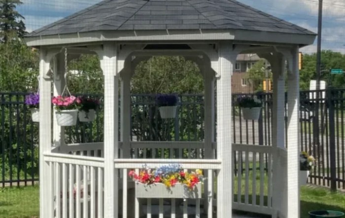 A quaint wooden gazebo adorned with colorful hanging flowers in a garden setting.