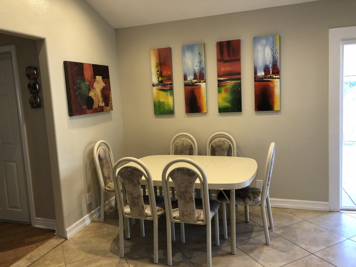 A cozy dining room with a table and six chairs, decorated with colorful abstract artworks on the walls.