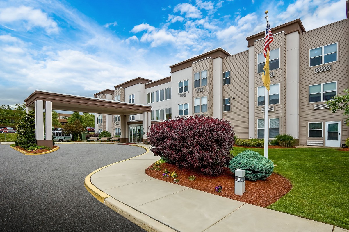 Exterior view of a hotel building with a driveway, landscaping, and flagpole.