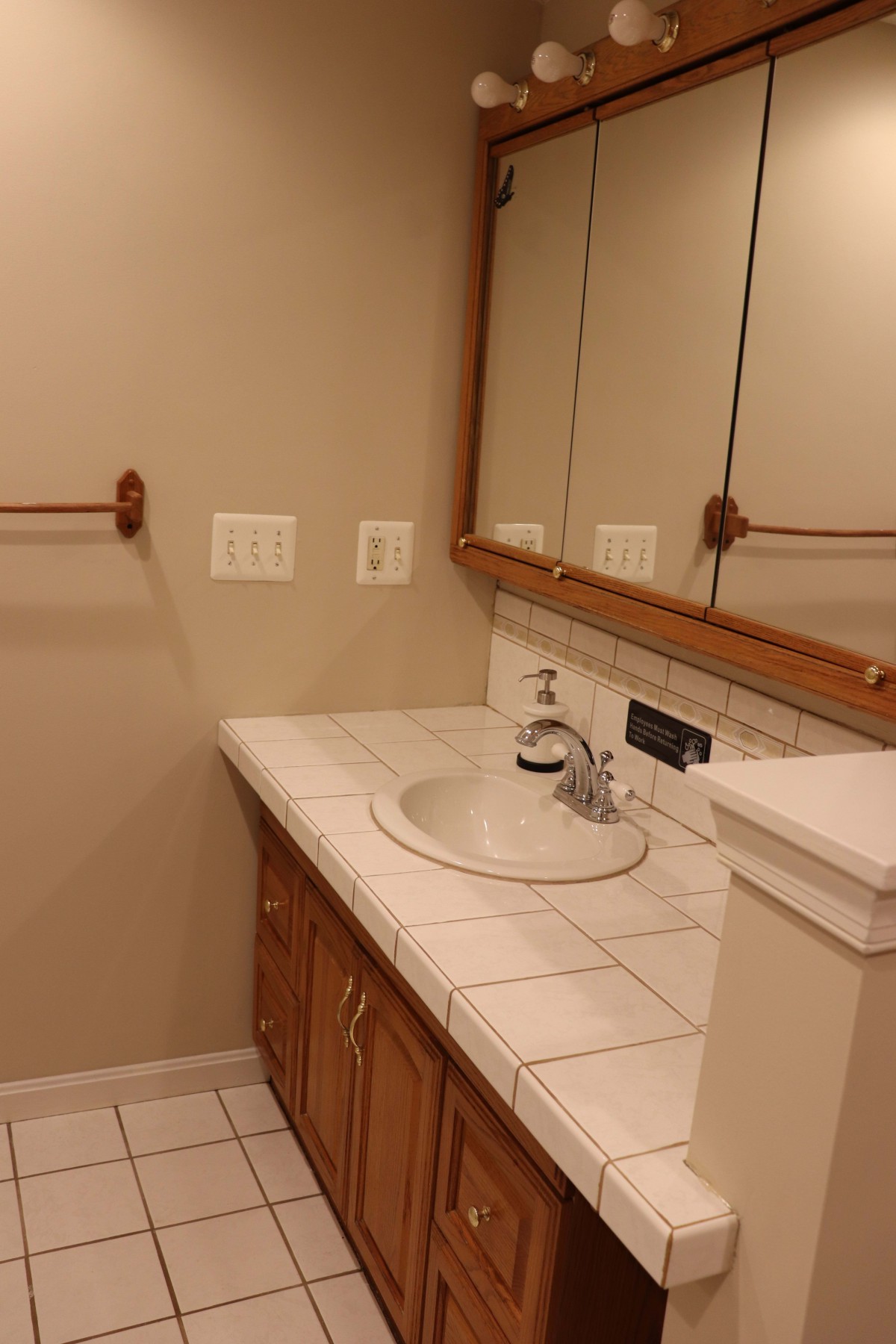 A bathroom with a tiled countertop, sink, and mirrored cabinet.