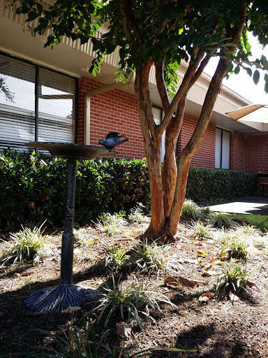 A peaceful garden scene featuring a tree, flowers, and a building in the background.