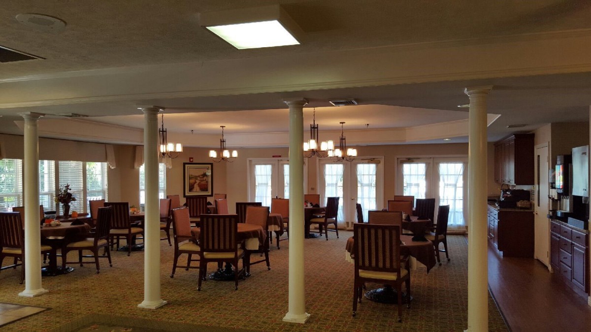 A spacious dining room with multiple tables and chairs, elegantly lit by chandeliers.