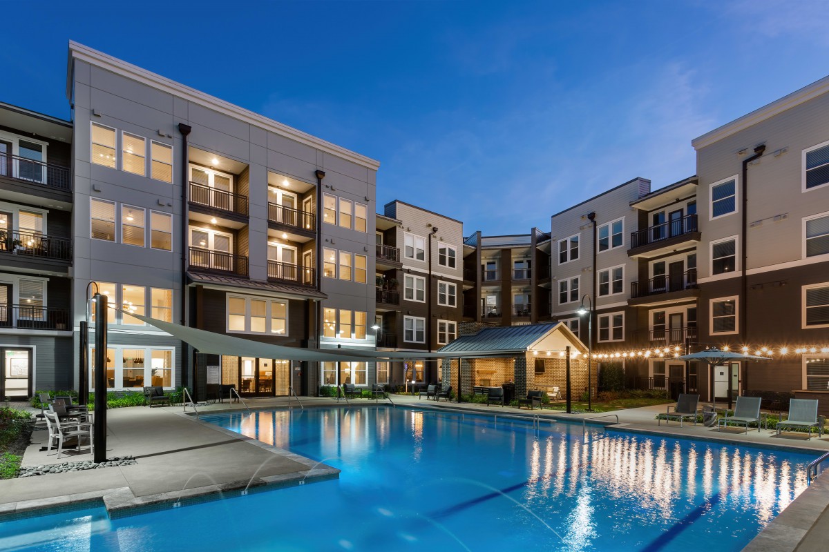 A modern apartment complex with a well-lit swimming pool during the evening.