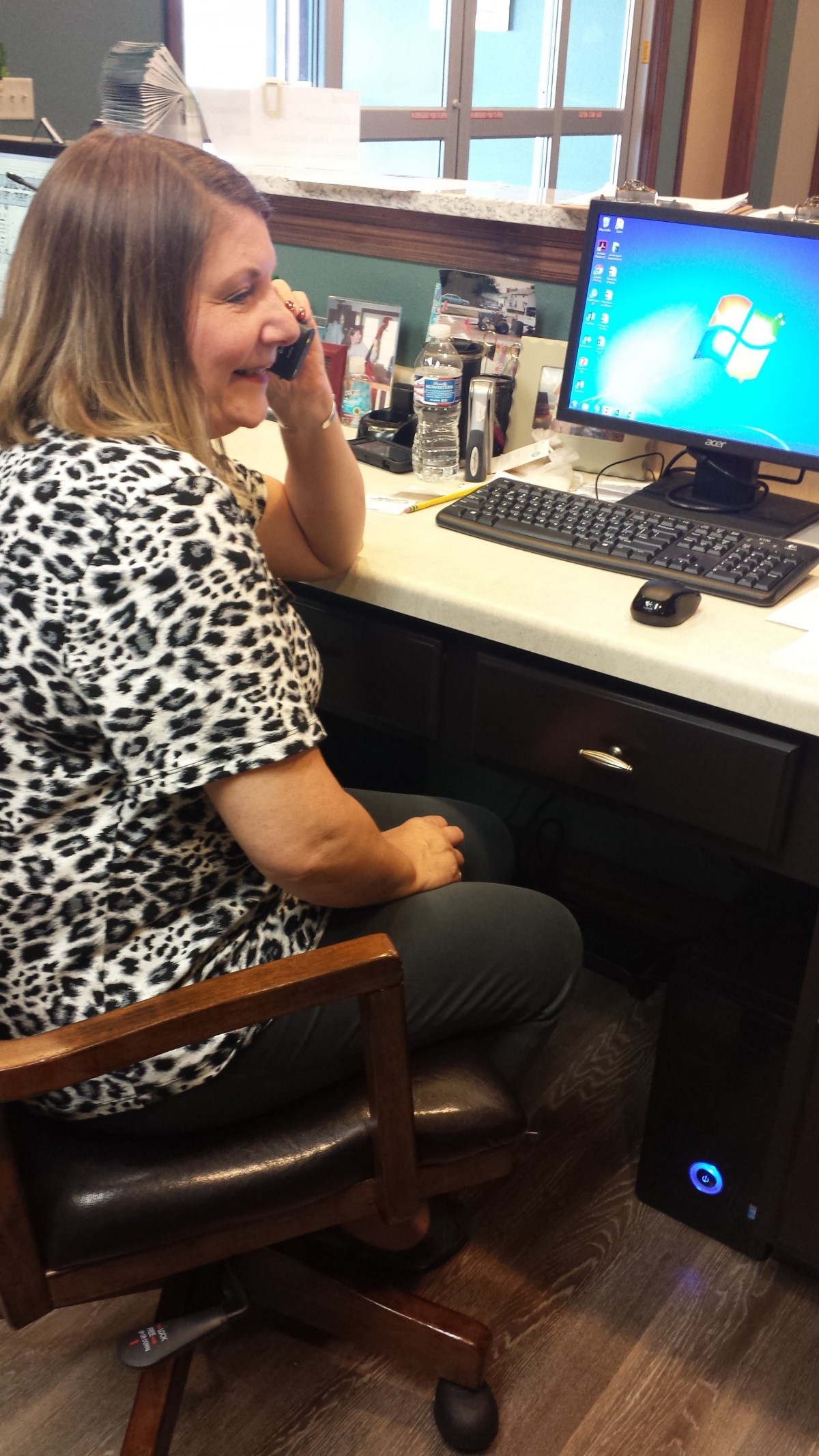 A woman in an office talking on the phone while using a computer.