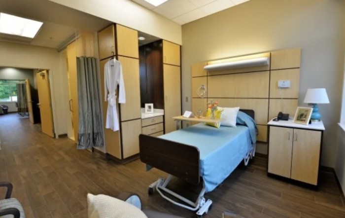 A modern hospital room featuring a single bed with blue linens, designed for patient comfort and care.