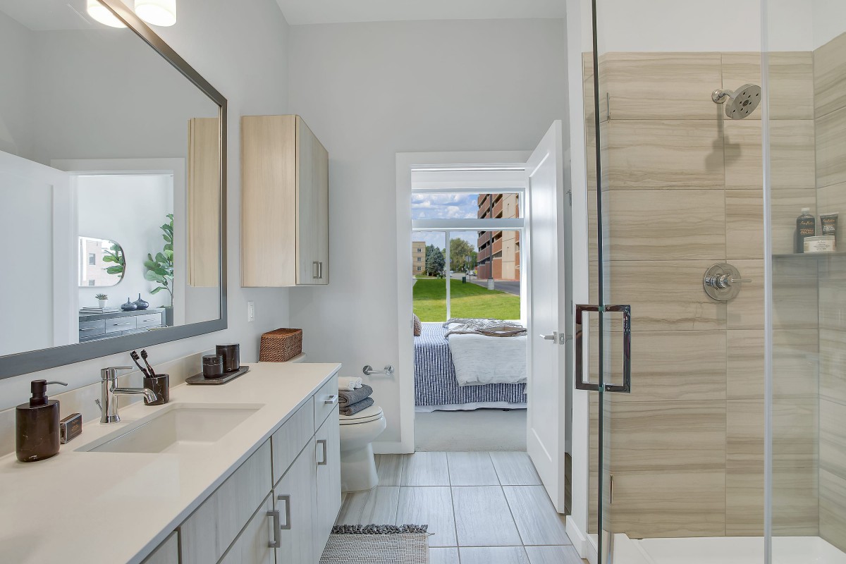 A modern bathroom with a spacious layout, featuring a sleek sink, large mirror, and a glass-enclosed shower.