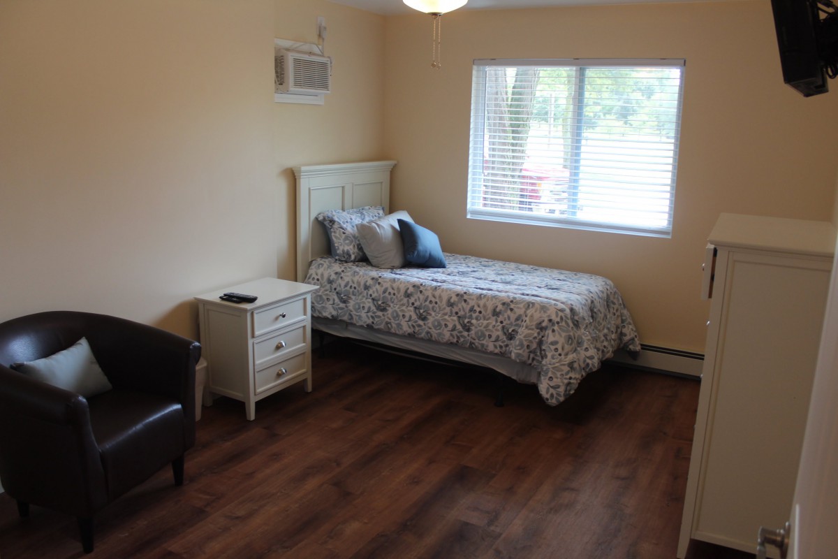 A cozy bedroom with a single bed, hardwood floors, and a window letting in natural light.