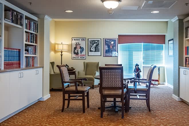 A cozy living room with a table and chairs, adorned with artwork on the wall and a bookshelf.
