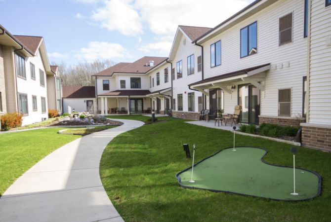A large residential building with a well-maintained lawn and concrete sidewalks under a sunny sky.