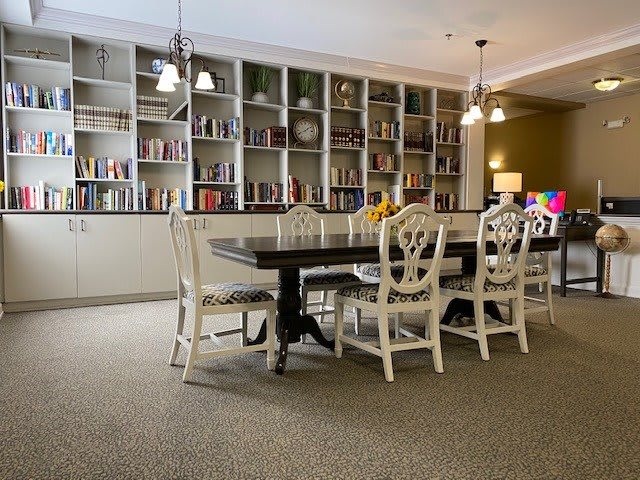 A cozy dining room with a long table, surrounded by chairs, adorned with pendant lights and lined with bookshelves.