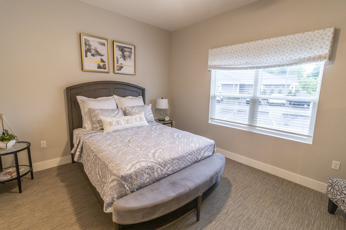 A cozy bedroom featuring a neatly made bed, wall art, and a large window with blinds.