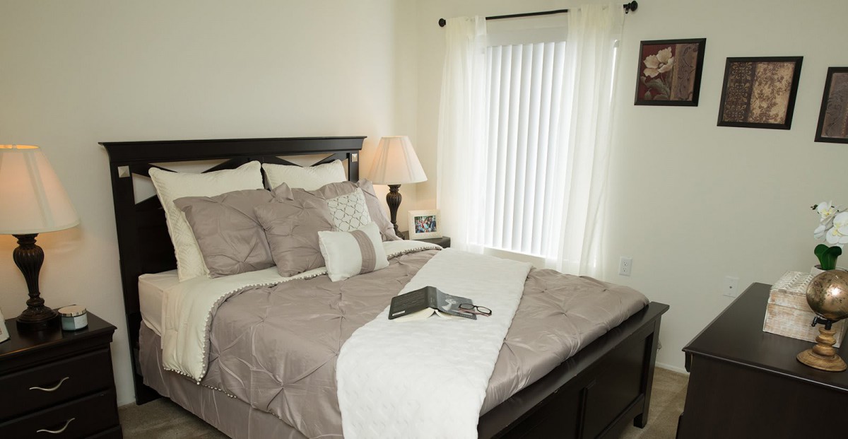 A cozy bedroom with a neatly made bed, soft pillows, a bedside lamp, and curtains filtering the light.