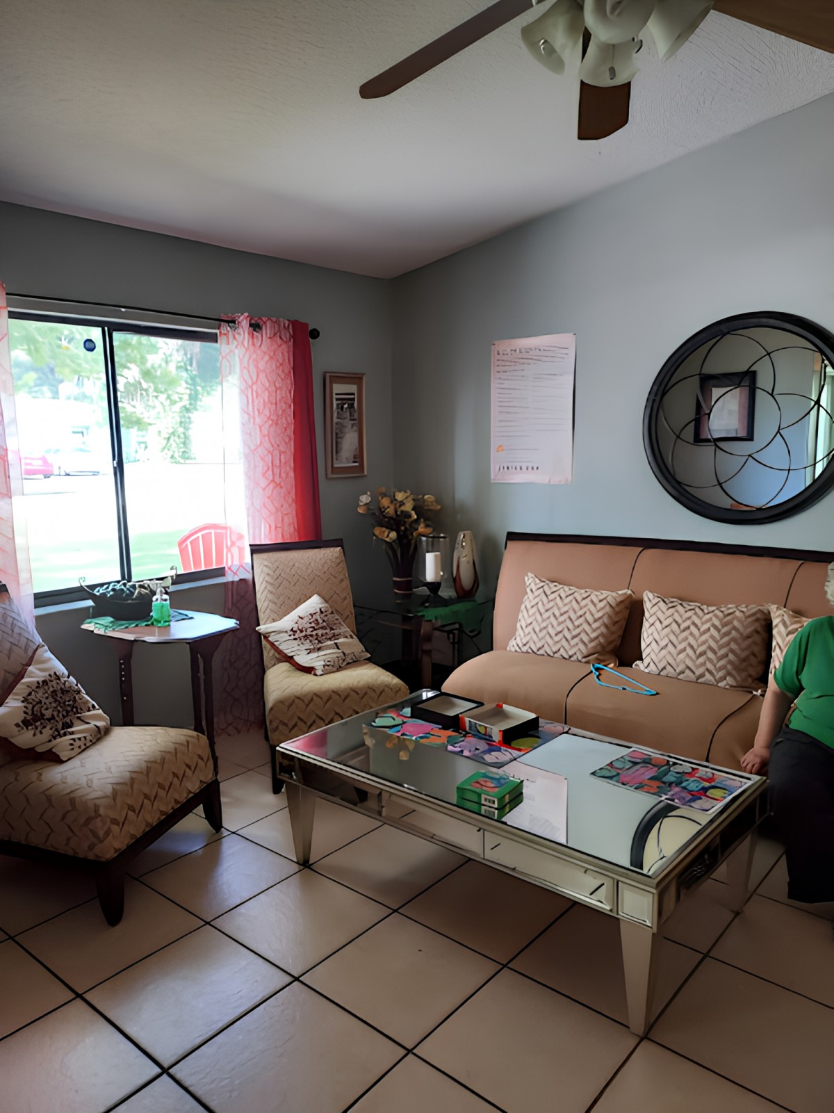 A cozy living room with a sofa set and a coffee table, complemented by decorative items and large windows.