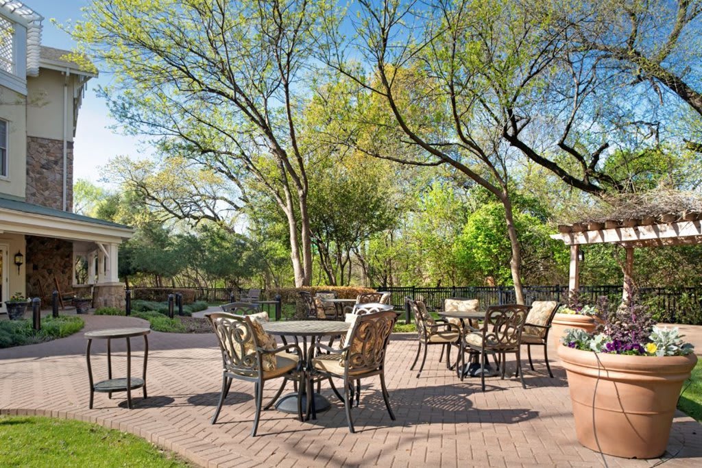 A tranquil outdoor patio area with tables and chairs surrounded by lush greenery.