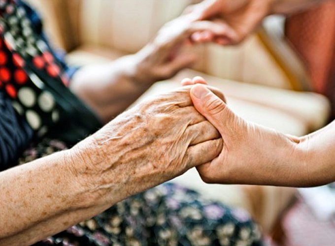 An elderly hand being held by another in a gesture of support and connection.