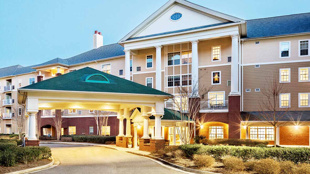 The image shows a well-lit hotel entrance with prominent columns and manicured landscaping.