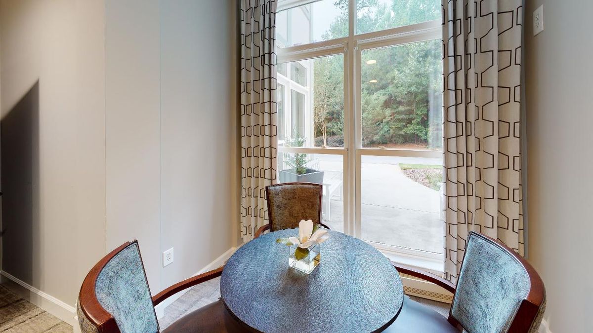 A cozy dining area with a round table set near a large window adorned with curtains, featuring a small plant decoration in the center.