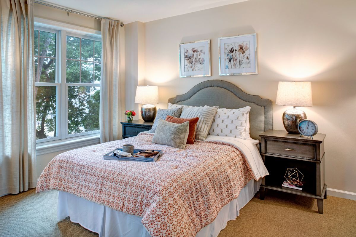 A cozy bedroom with a neatly made bed, flanked by two lamps, and decorated with artwork above the headboard.