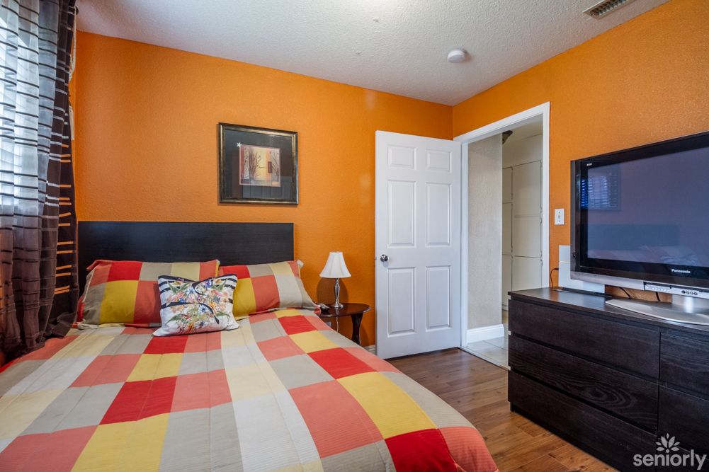A cozy bedroom with orange walls, a colorful bedspread, and modern furnishings.