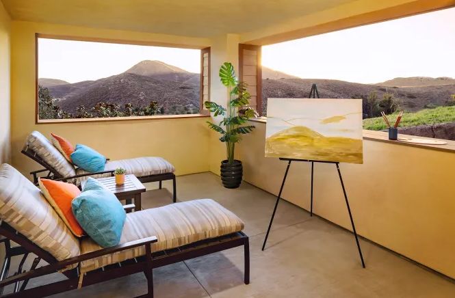 A peaceful balcony setup with reclining chairs, a scenic mountain view, and an art easel displaying a painting.