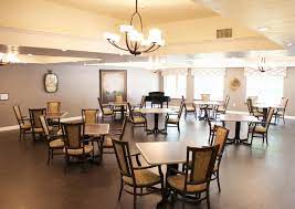 A well-lit dining area featuring multiple tables and chairs, a chandelier, and a piano in the corner.